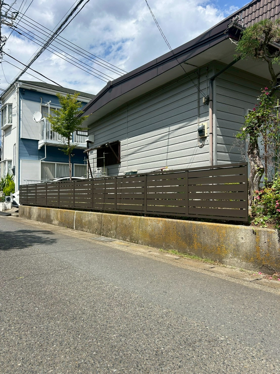 海老名市で行われたリフォーム後の住宅外構。生垣を撤去し、既存擁壁に設置されたLIXIL(リクシル)の目隠しフェンス(フェンスAB YS3型)。採光と採風を両立した横スリットデザインで、外壁とも調和する洗練された雰囲気。 海老名市で行われたリフォーム後の住宅外構。生垣を撤去し、既存擁壁に設置されたLIXIL(リクシル)の目隠しフェンス(フェンスAB YS3型)。採光と採風を両立した横スリットデザインで、外壁とも調和する洗練された雰囲気。