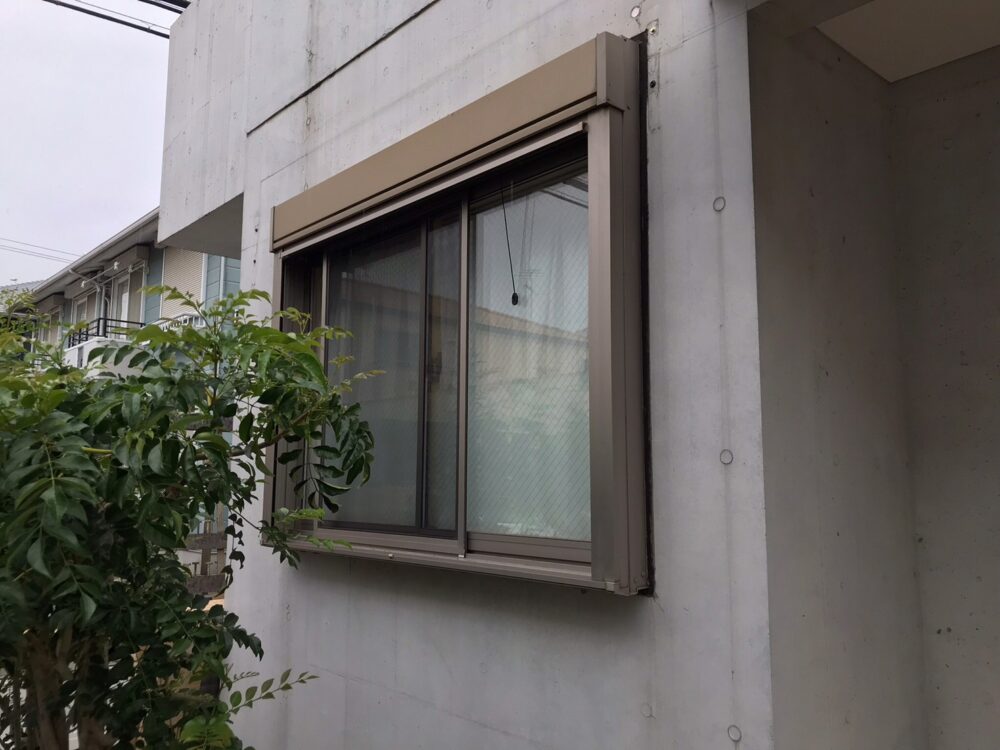 海老名市の住宅。外からの視線が気になるシャッター付き窓の施工前。庭の植栽越しの風景。