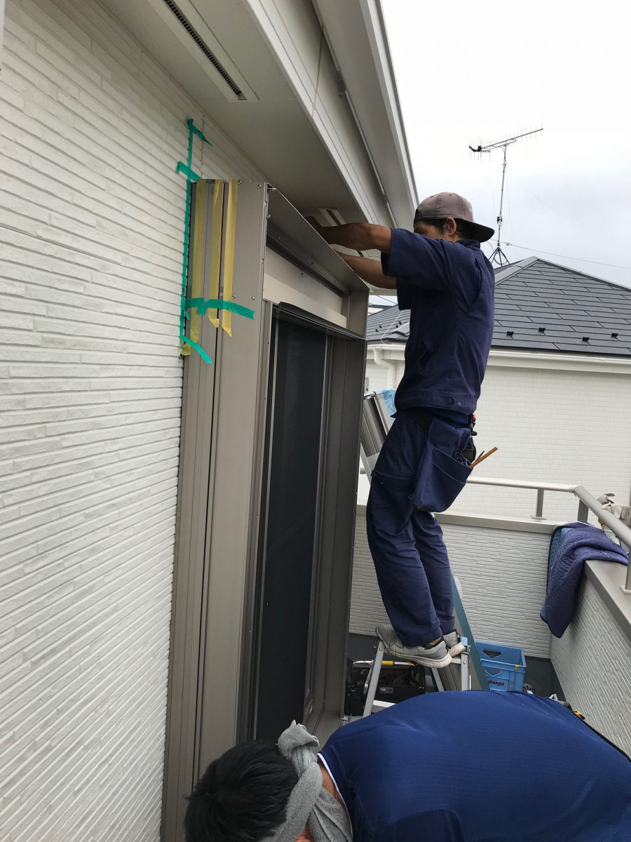 窓に設置されたLIXILリフォームシャッターの後付け専用枠に本体ボックスを固定する職人の様子 窓に設置されたLIXILリフォームシャッターの後付け専用枠に本体ボックスを固定する職人の様子